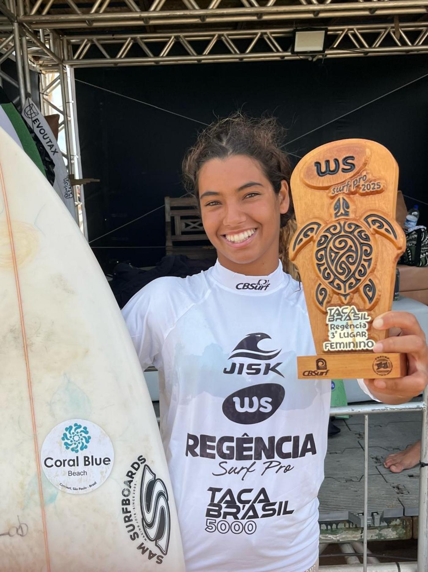 jovem surfista mulher mostra prancha e troféu #paratodosverem