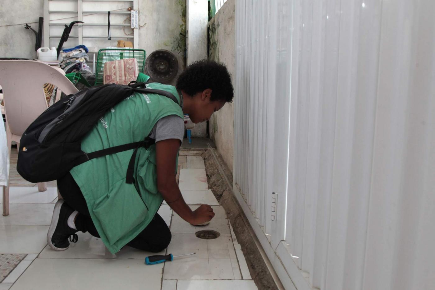 Agente de combate à dengue está agachada observando ralo. #Paratodosverem