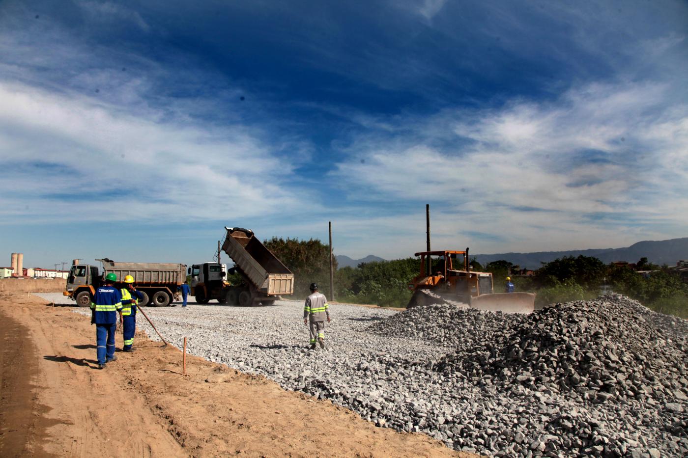 operários e caminhões durante construção da via #pracegover 