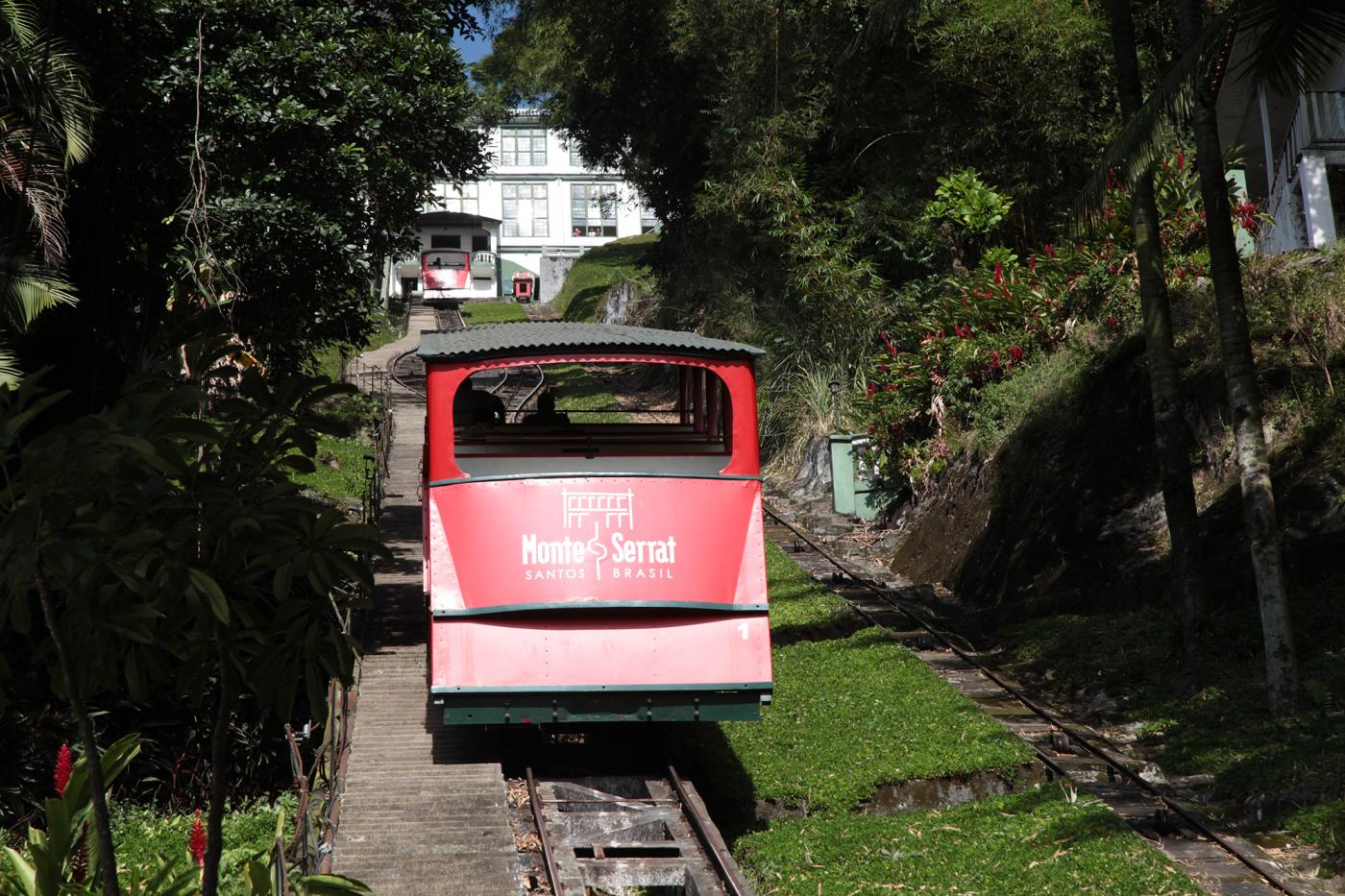 Bonde funicular percorrendo trilho no morro em meio a vegetação. #Pracegover