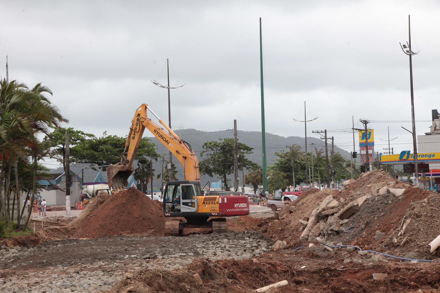 Trator está na pista movimentando terra. Área tem pedra e montes de areia e pedra. #Pracegover