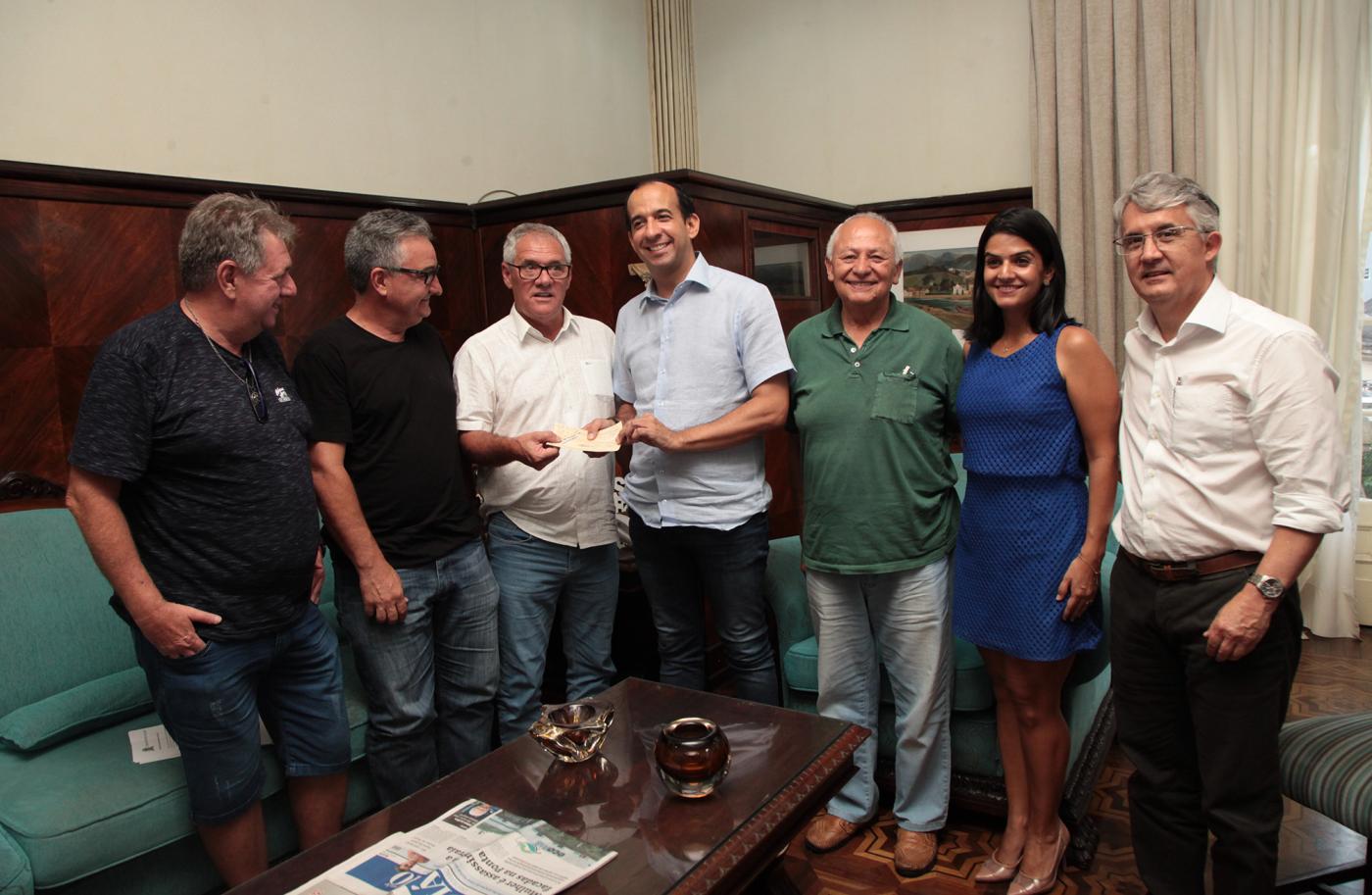 Prefeito e presidente da Câmara lado a lado, este com chequ nas mãos. Outros vereadores estão em volta. #Pracegover