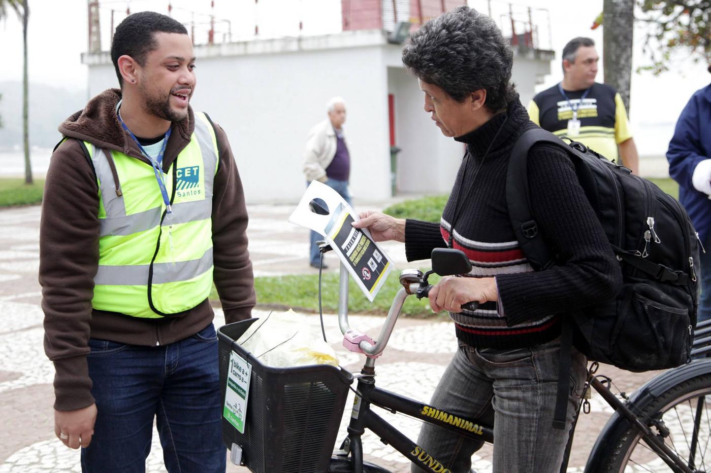 agente entrega folheto a ciclista #pracegover 