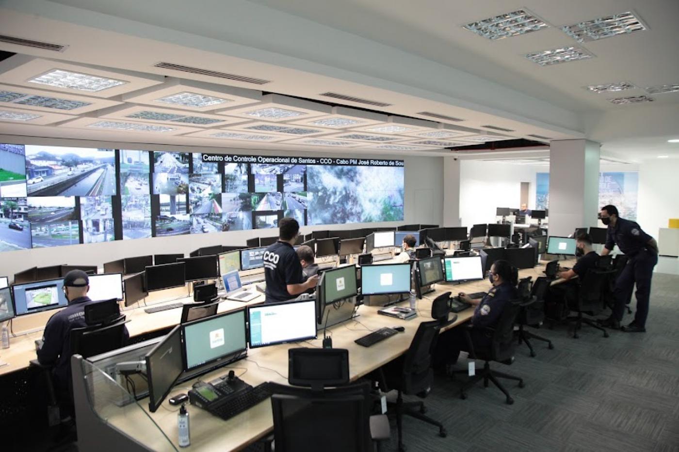 Centro de controle operacional com vários computadores e várias telas com imagens das câmeras. #paratodosverem