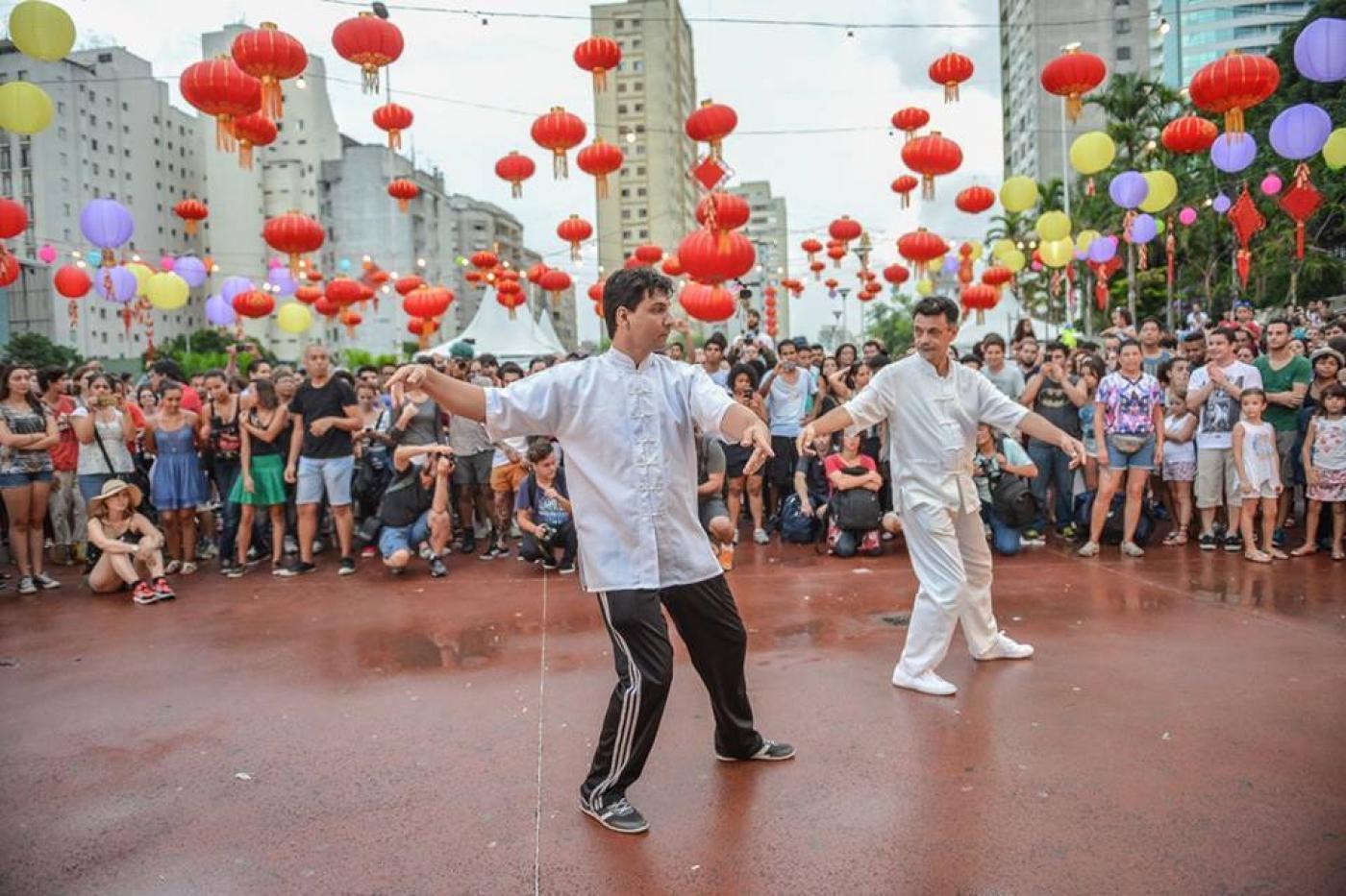 duas pessoas praticam tai chi em área decorada por balões. #paratodosverem