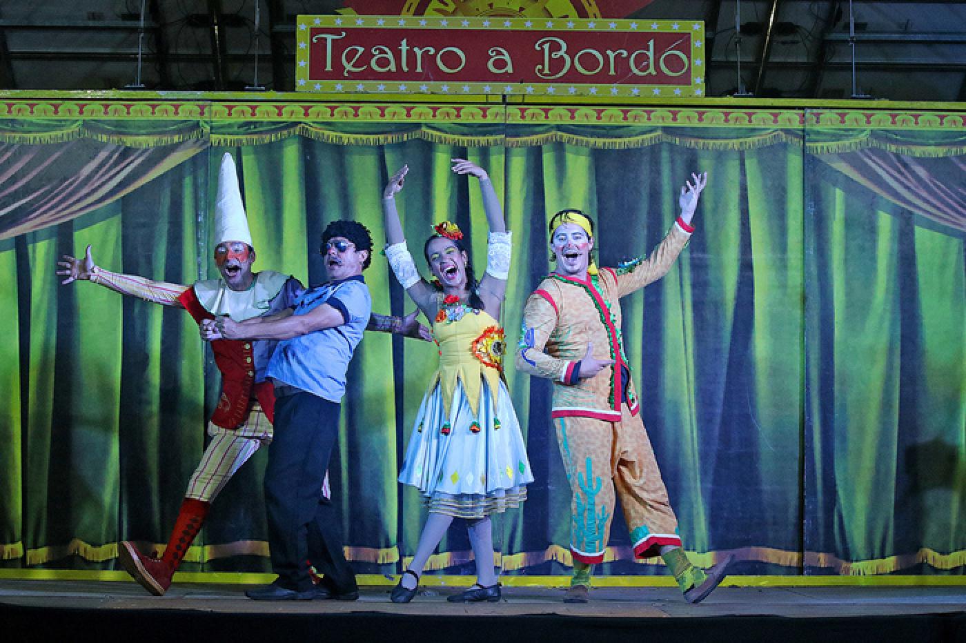 QUATRO ATORES VESTIDOS DE PALHAÇOS ESTÃO NO PALCO. CORTINA AO FUNDO. NO ALTO SE LÊ TEATRO A BORDO. #PARATODOSVEREM