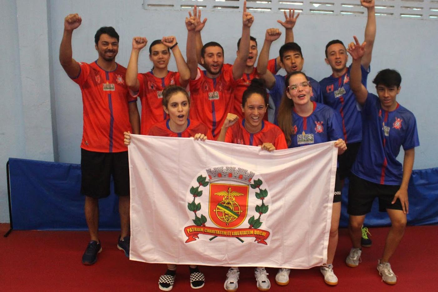 atletas erguem as mãos e seguram bandeira de santos #paratodosverem