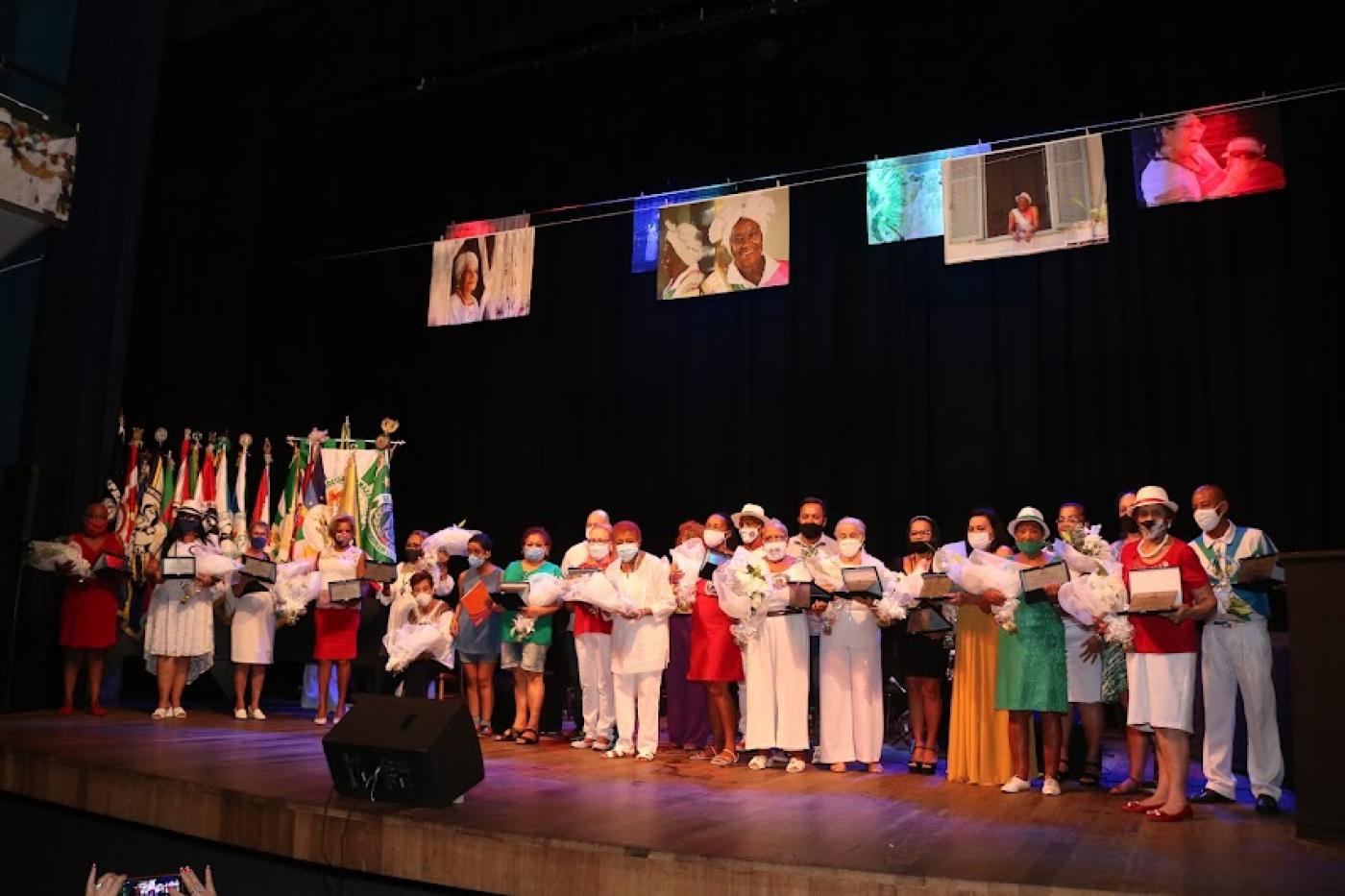 Homenageadas em cima do palco com flores #paratodosverem