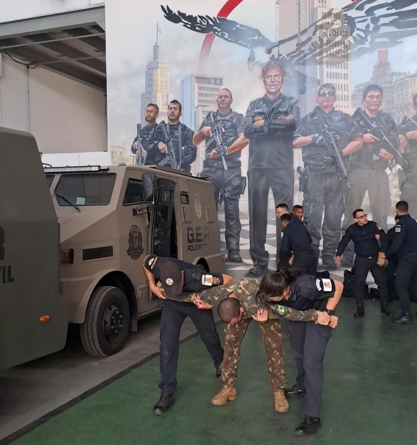 homem com roupa camuflada simula ação enquanto é contido por dois guardas. #paratodosverem 