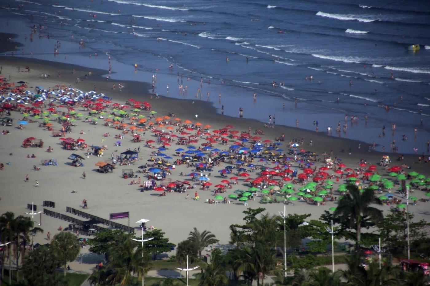 Vista aérea de praia com vários guarda sois abertos. #paratodosverem