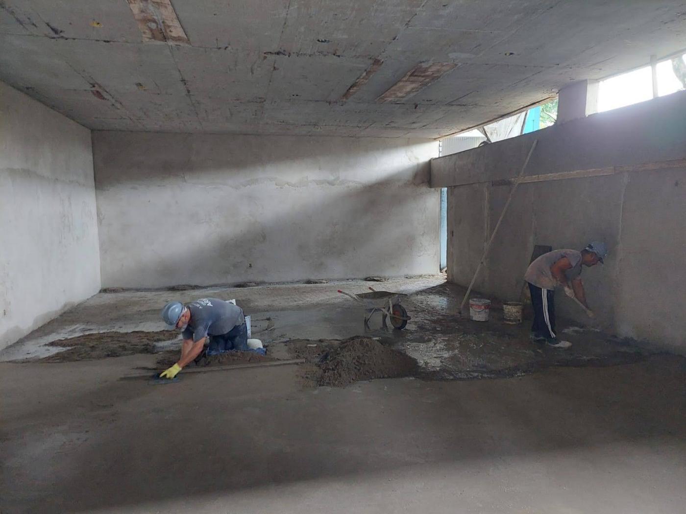 homens trabalham na aplicação de contrapiso em sala. #paratodosverem