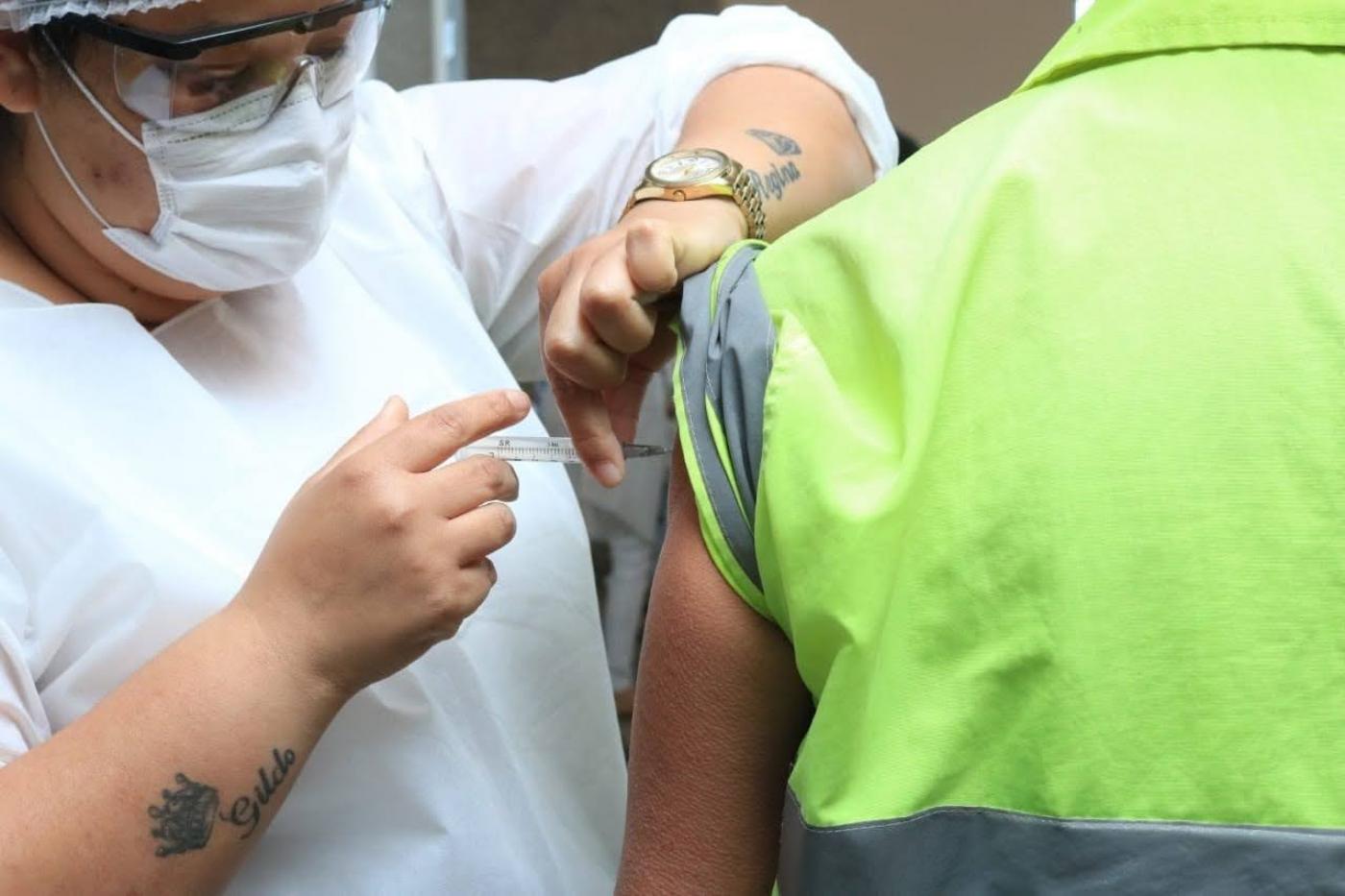 mulher vacina homem que usa uniforme com faixa reflexiva. #paratodosverem