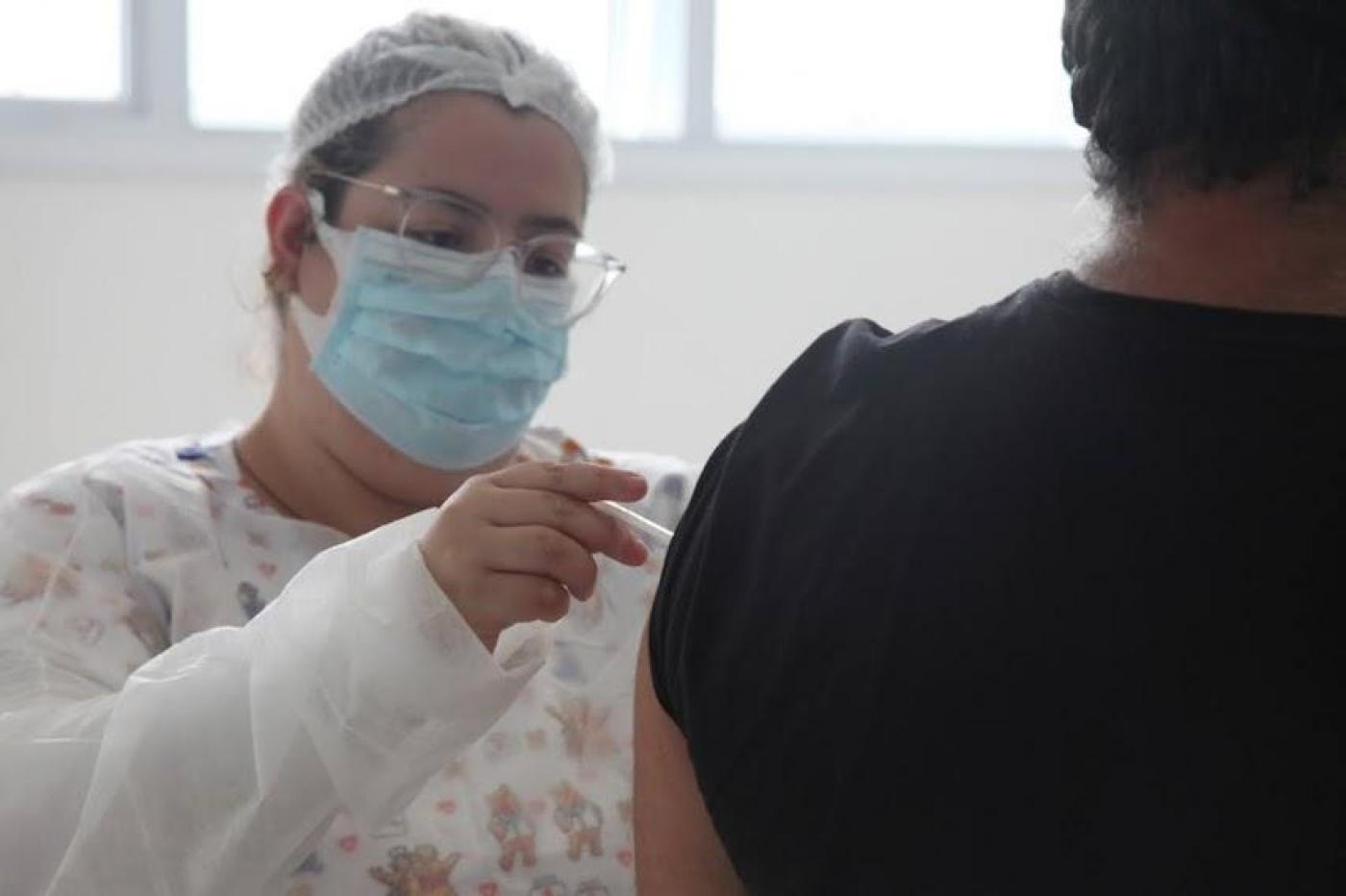 Enfermeira aplica vacina em braço de homem. #paratodosverem