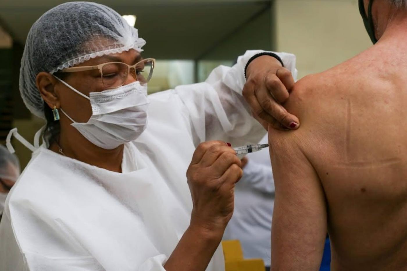 mulher usando avental, touca e máscara vacina homem. #paratodosverem