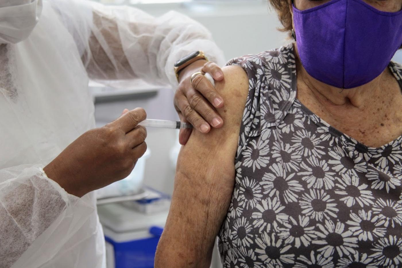 Mãos vacinam braço de mulher. Imagem em close. #Paratodosverem