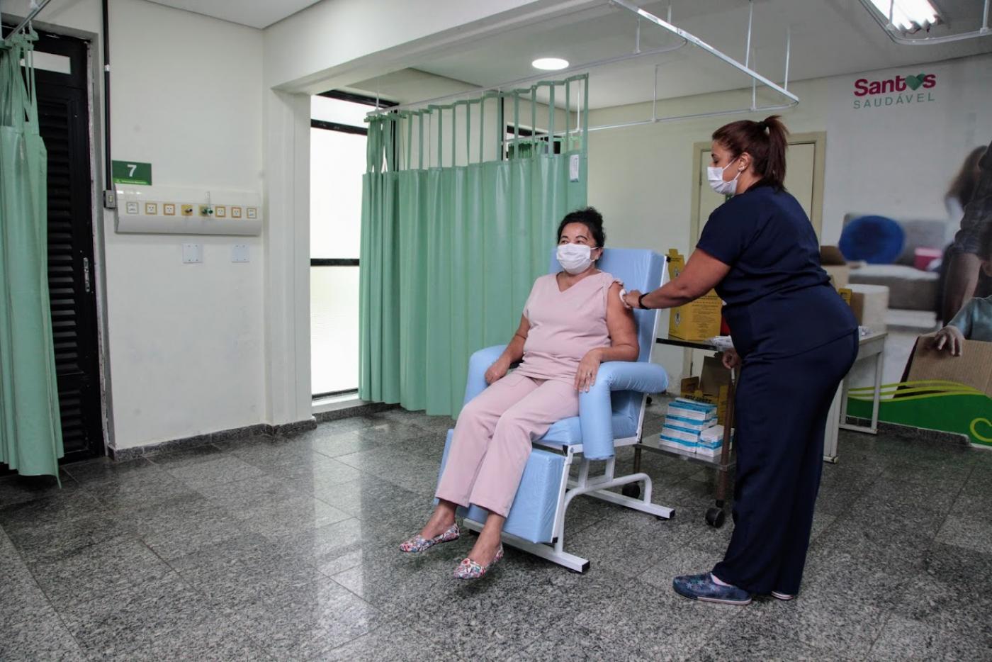 Mulher está sentada sendo vacinada. #Paratodosverem