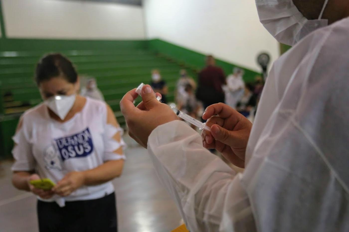 enfermeiro prepara aplicação da vacina e mulher mexe no celular #paratodosverem