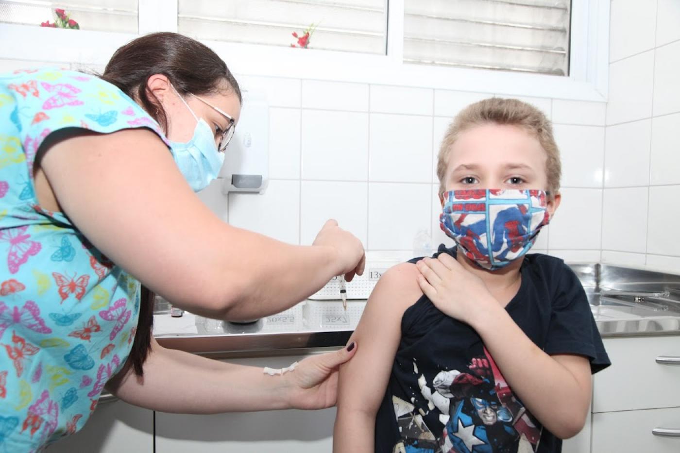 Menino recebe injeção no braço aplicada por profissional de saúde. #paratodosverem
