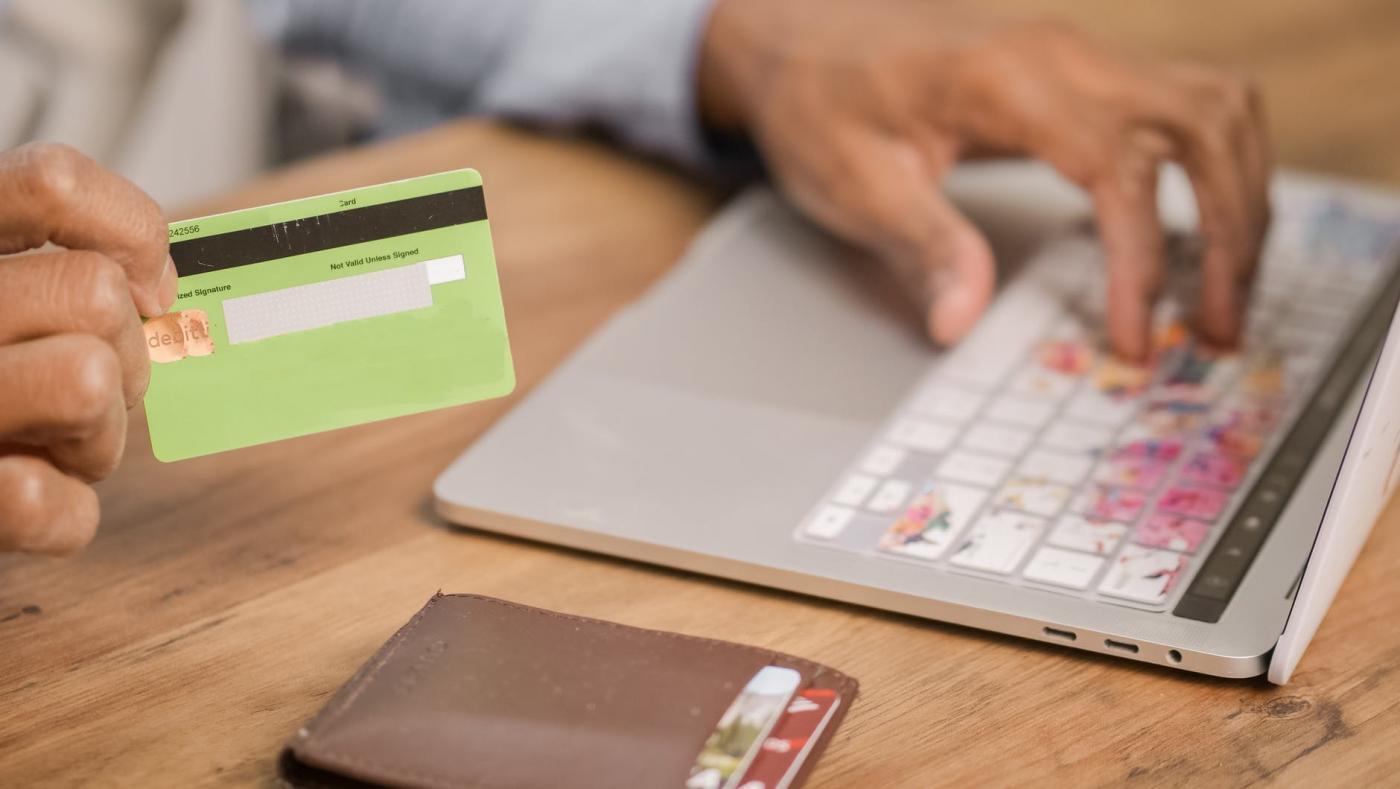 mão segura cartão de compras enquanto outra digita em notebook. #paratodosverem