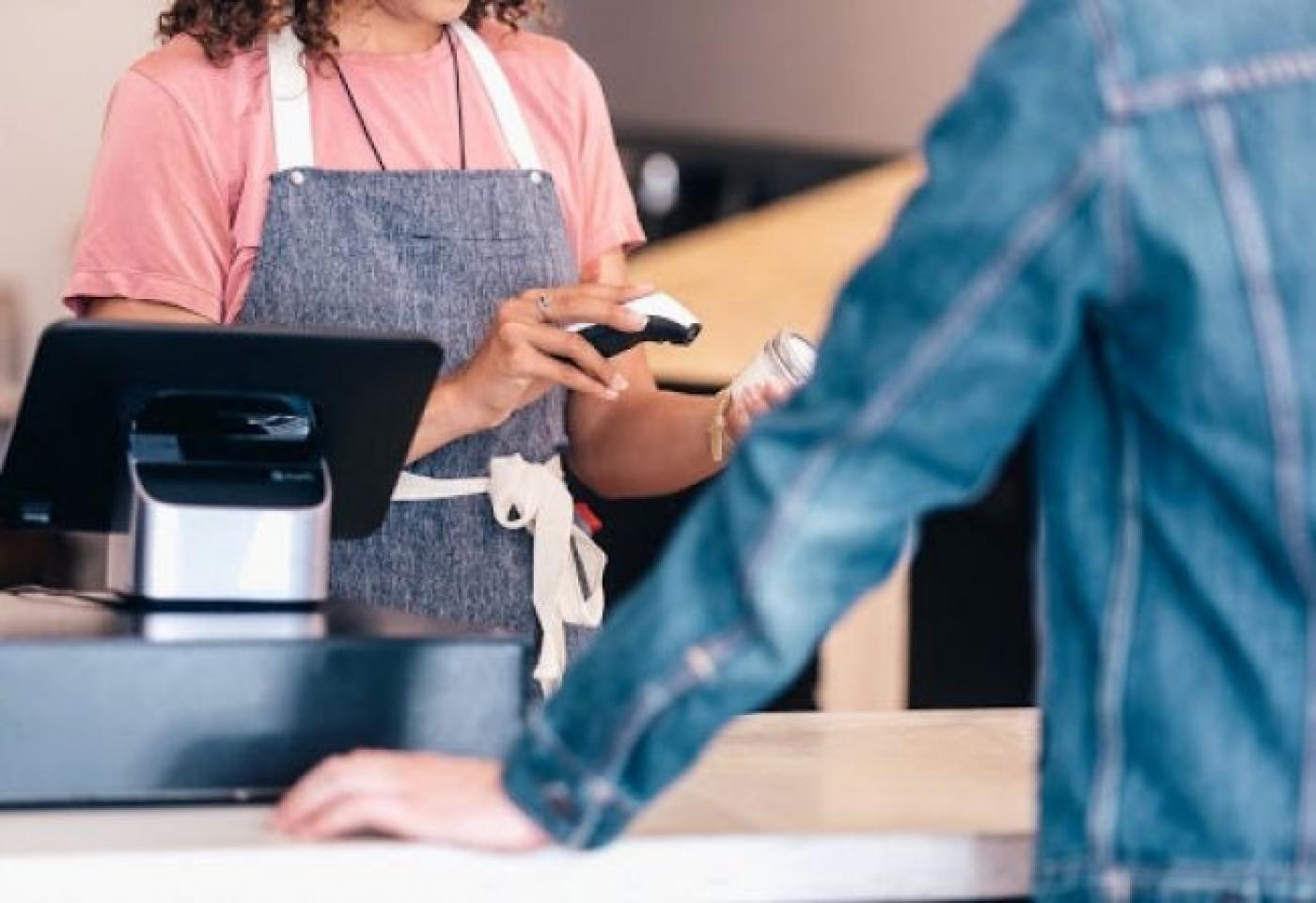 caixa de mercado está passando o scanner em produto. Há um cliente  na frente dela. #paratodosverem