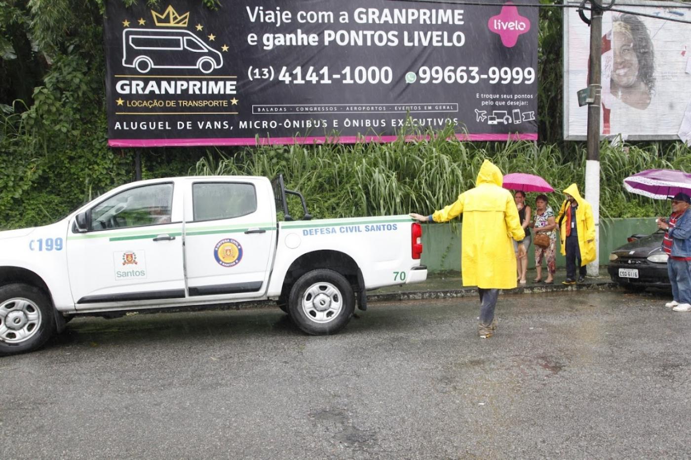 viatura da defesa civil em área de risco em dia de chuva. Agentes com capas amarelas estão na área. #paratodosverem