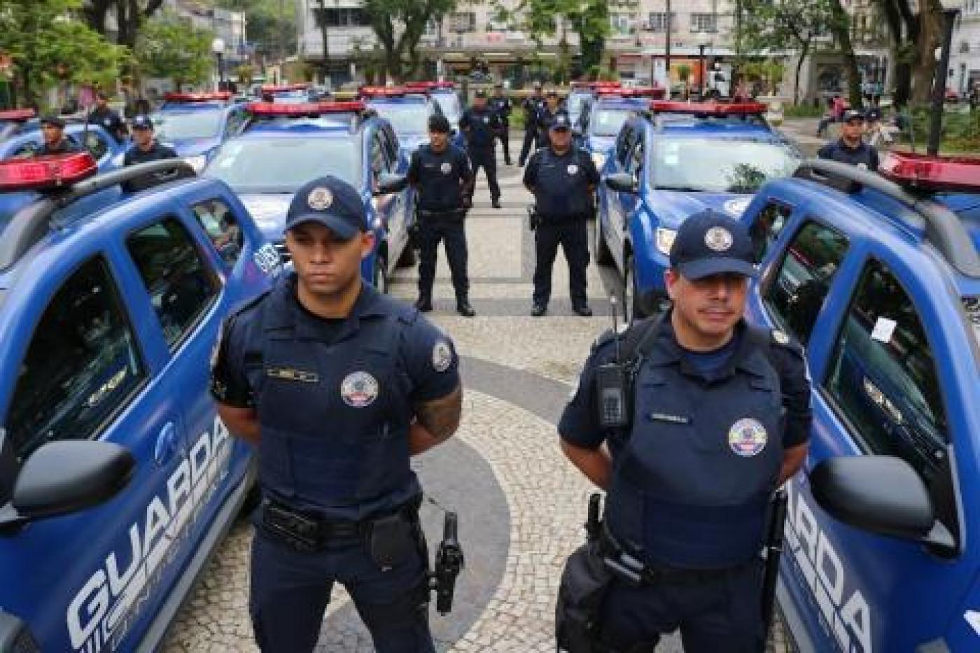 guardas municipais estão em posição de sentido, ao lado de viaturas. #paratodosverem 