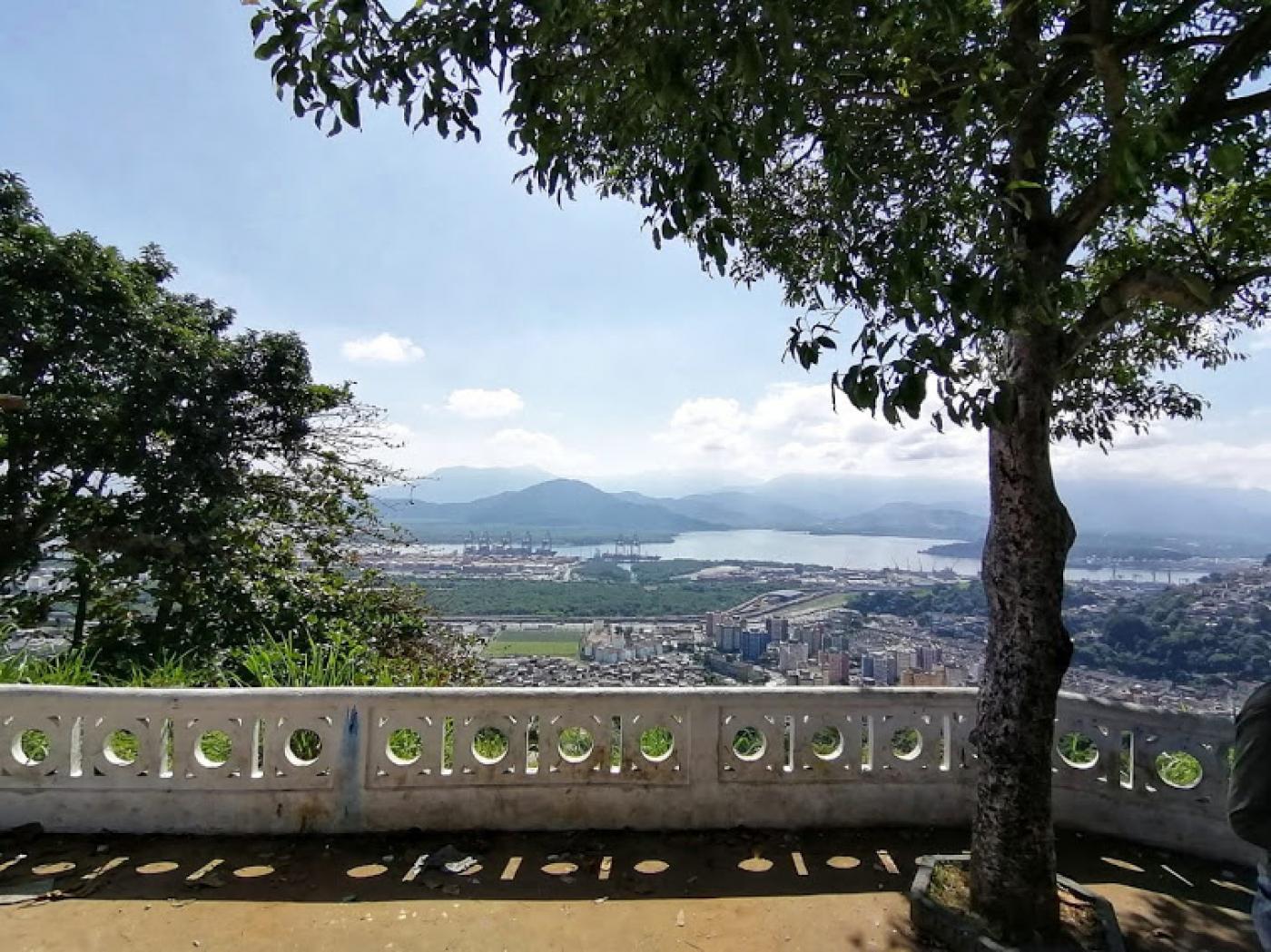 Vista da cidade a partir do alto da Vila Progresso. Em primeiro plano, uma árvore à direita e uma mureta com o formato tradicional de Santos. #paratodosverem