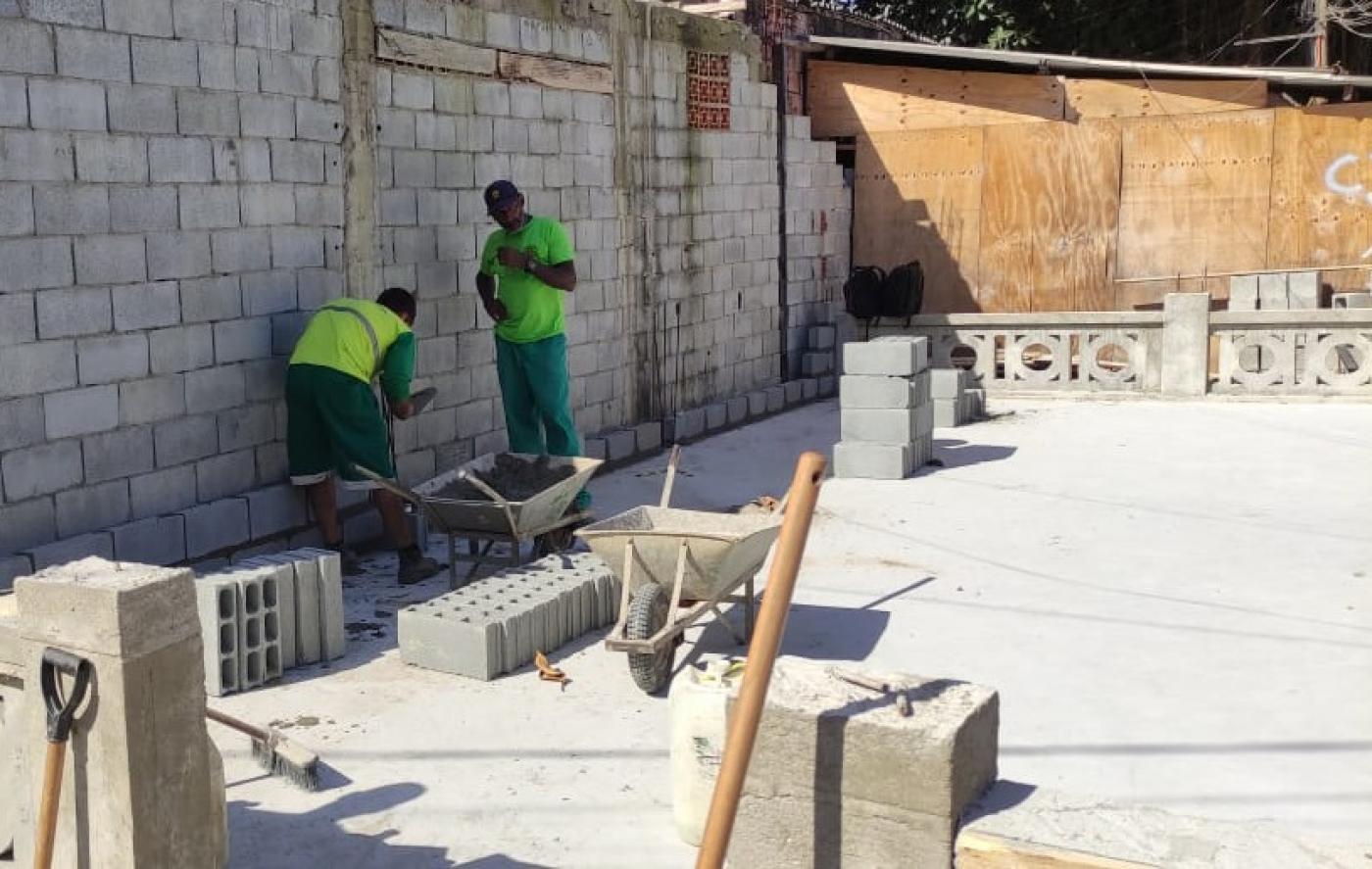 Operários empilham lajotas em obra de construção de parque infantil. #pracegover