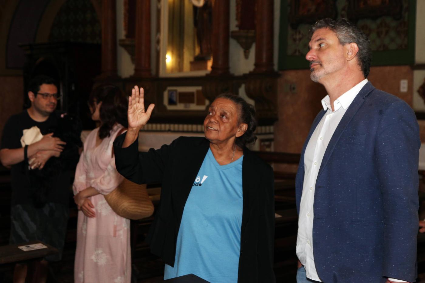 mulher uniformizada mostra ambiente de igreja para homem. #paratodosverem