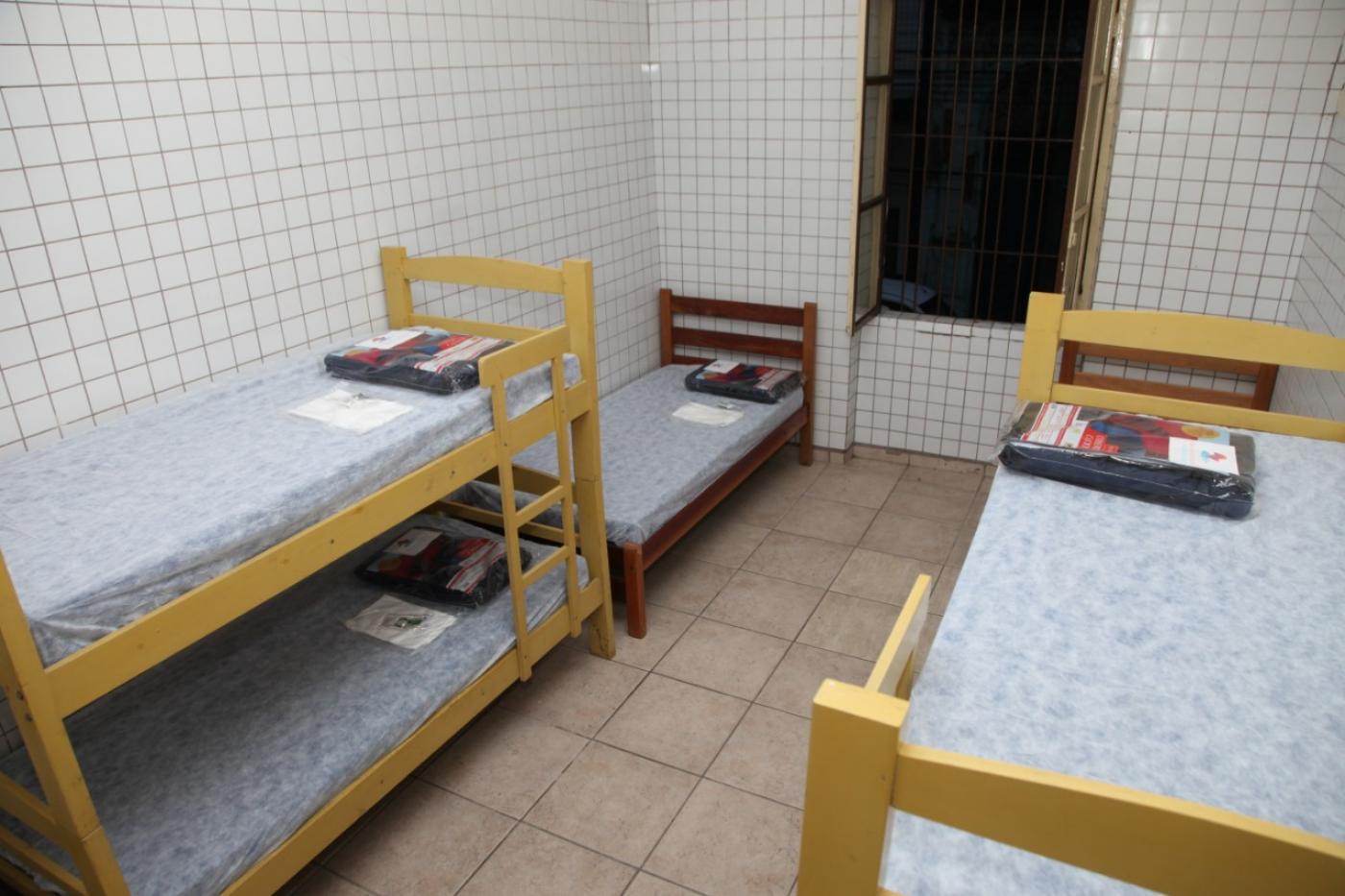 Quarto com camas beliche e uma individual. Todas as camas têm lençol e pacotes com cobertores. #Pracegover