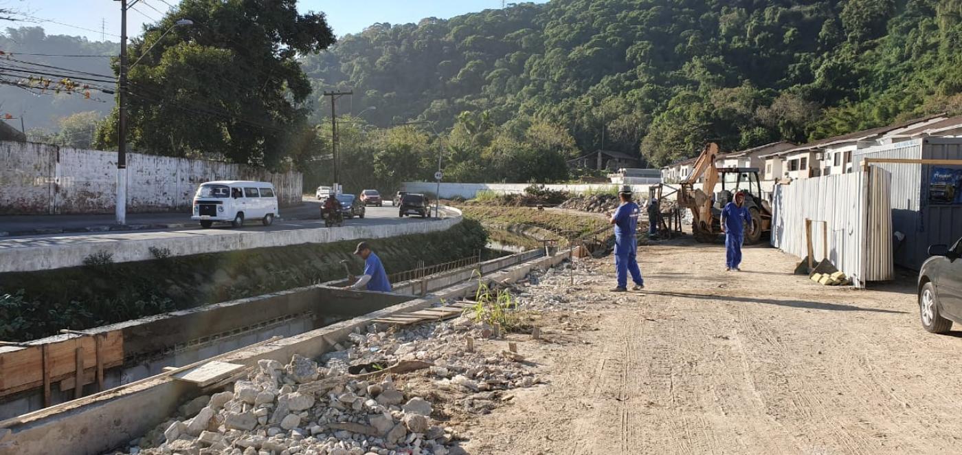 Homens preparam novo trecho de pista para concretagem ao lado de canal. #Pracegover