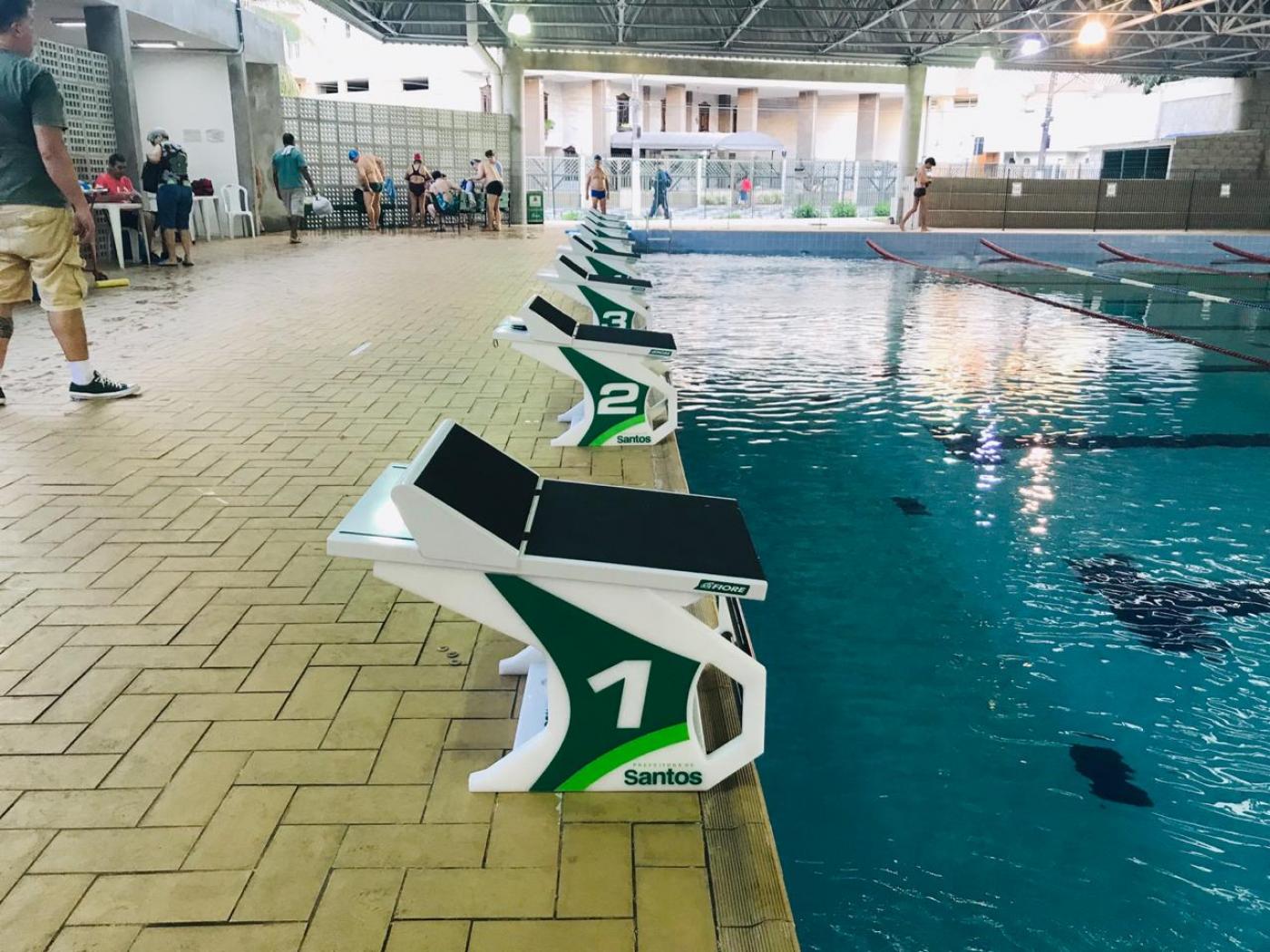 Blocos de partida em padrão específico para competições estão instaladas na beira da piscina. #Pracegover