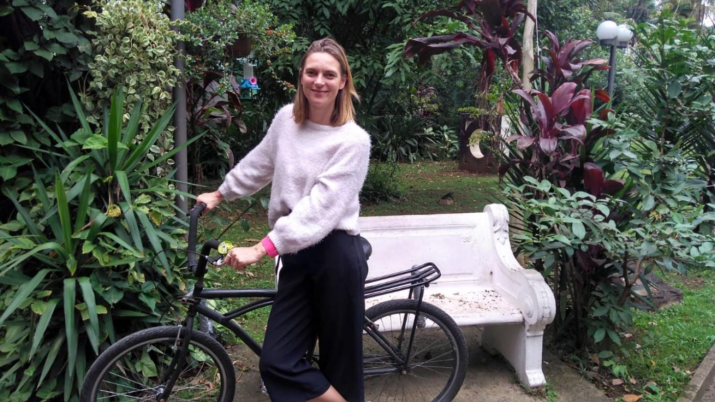 Kathrin Grund está em um jardim em pé e segurando o guidão de uma bicicleta. 