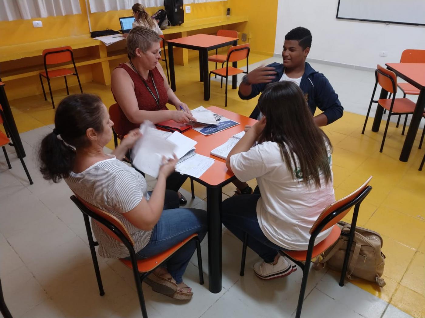 Alunos, representante da Ouvidoria e da equipe escolar estão sentados em torno de uma mesa. #Pracegover