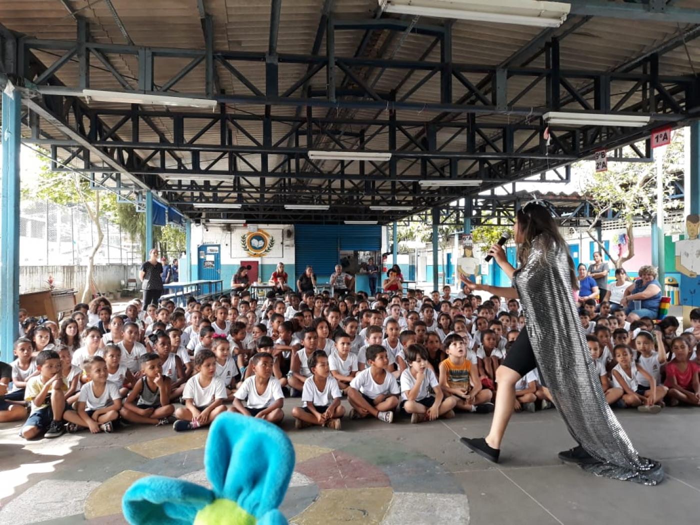 Artistas fazem apresentação para crianças em grande galpão. #Pracegover