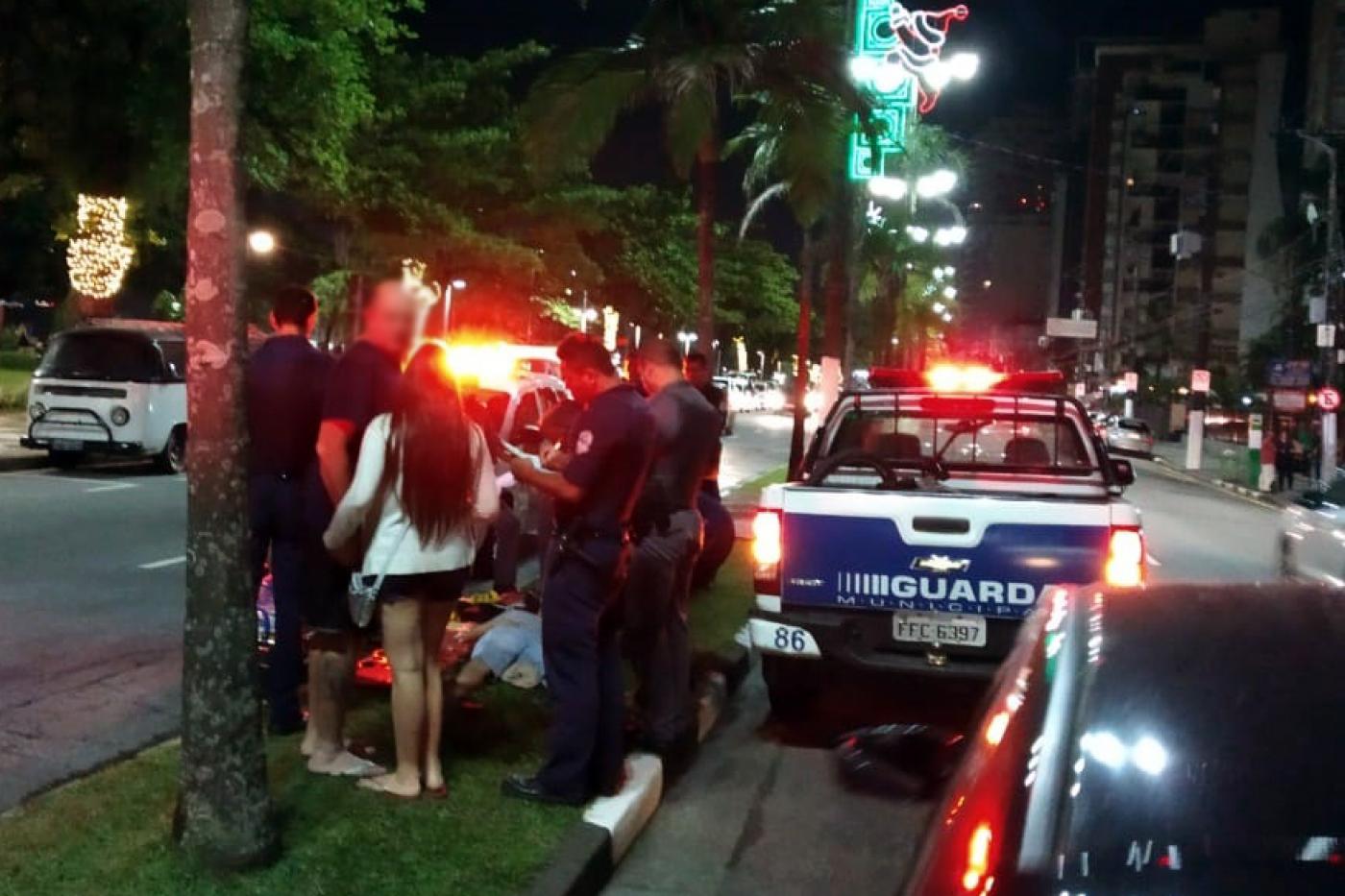 Dois socorristas, dois homens e uma mulher observam homem deitado no canteiro central da avenida da orla