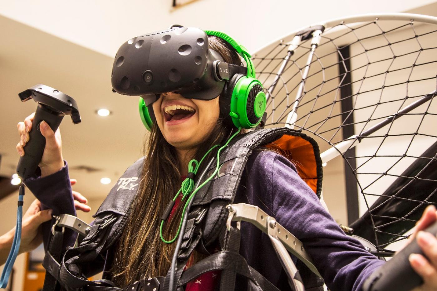 Menina está em um simulador de paramotor e tem nos olhos um óculos de realidade virtual. #Pracegover