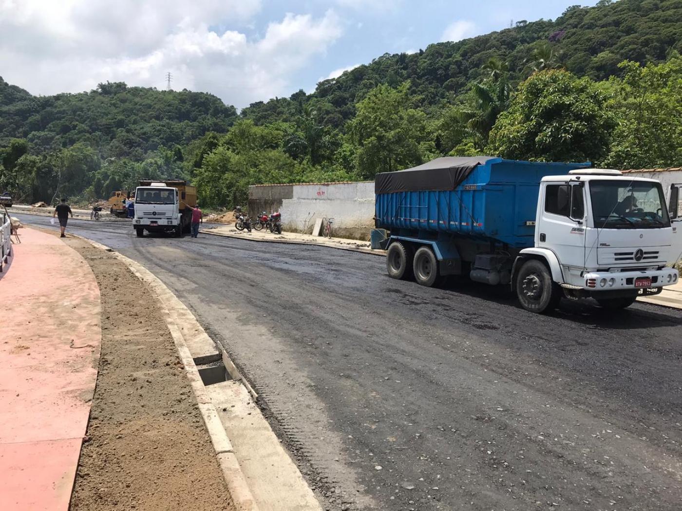 Vista geral de pista alfaltada. Ao lado direito se vê dois caminhões. Do esquerdo, o trecho de uma ciclovia. #paratodosverem