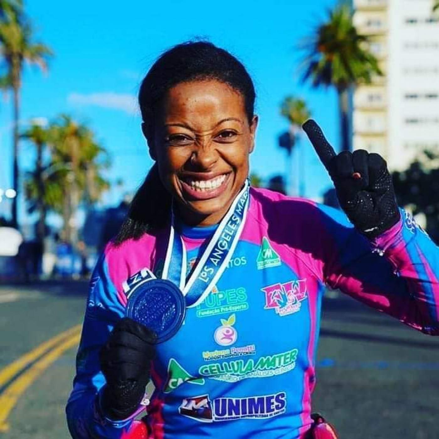 A paratleta Vanessa Cristina de Souza segura medalha no peito e sorri para foto. #Paratodosverem