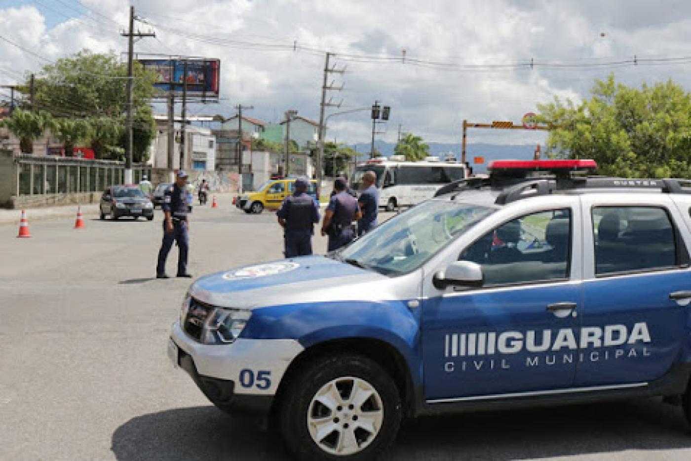 Veículo da Guarda Municipal em primeiro plano, guardas municipais e uma viatura da CET ao fundo, todos controlando o acesso em uma rua. #Paratodosverem