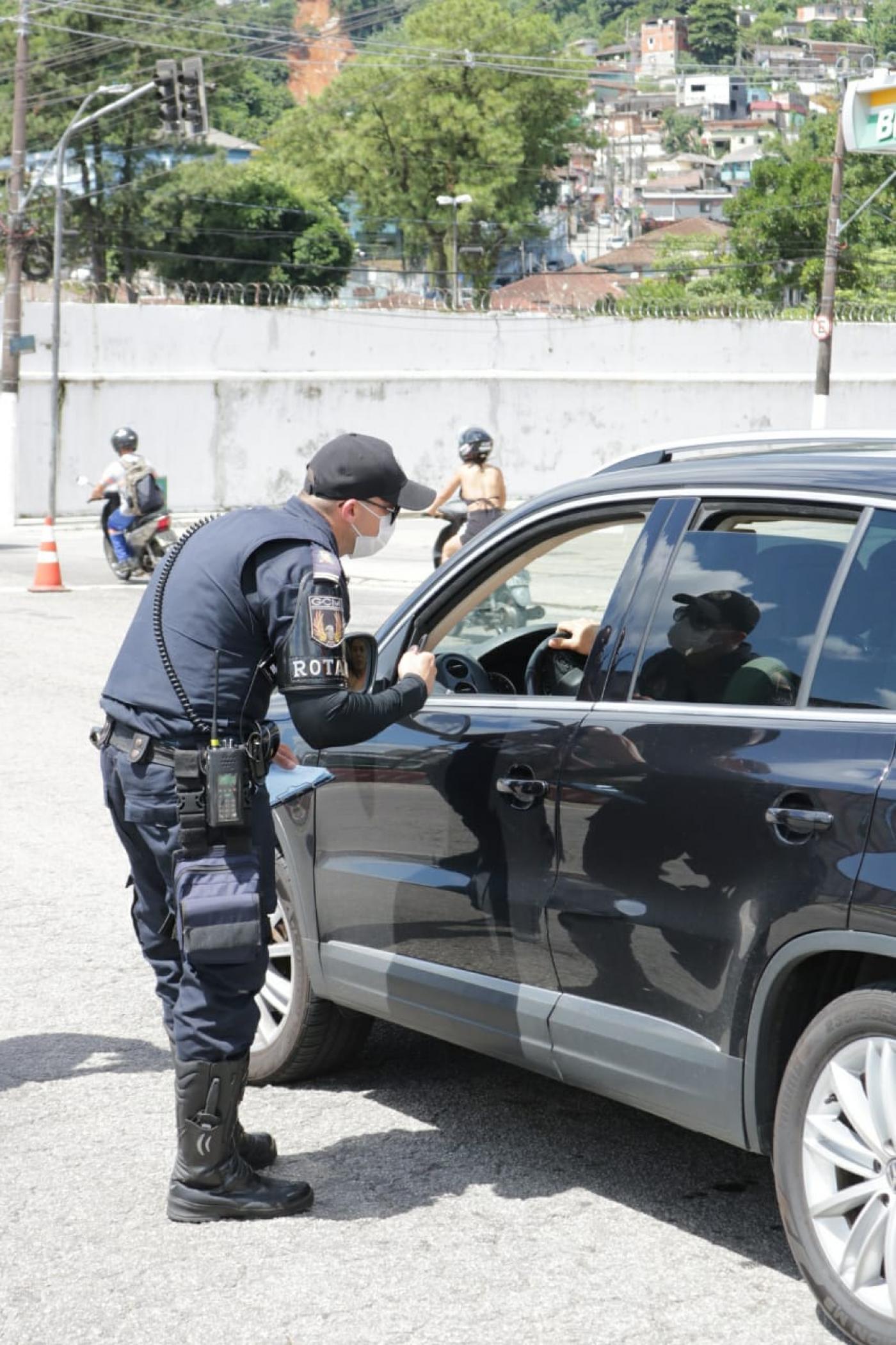 #pracegover Uniformizado, guarda municipal conversa com motorista dentro de carro em rua bloqueada por cones