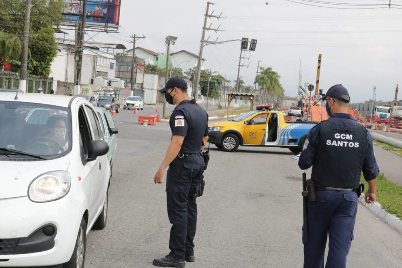 #pracegover em avenida, Dois guardas municipais abordam motorista dentro de carro, com veículo da C.E.T. ao fundo 