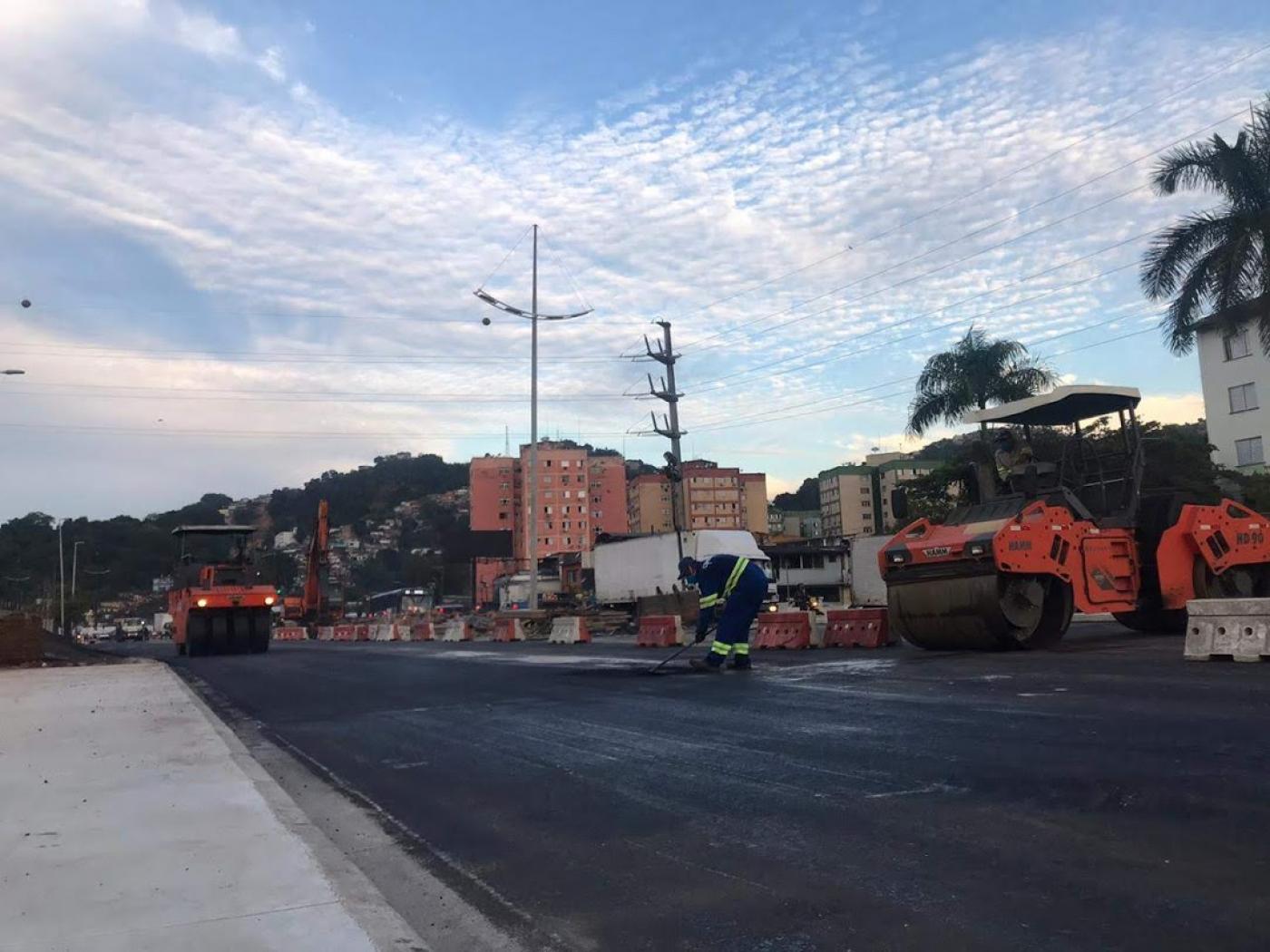 Trecho de pista recém-pavimentada, com máquina compactadora. #Paratodosverem