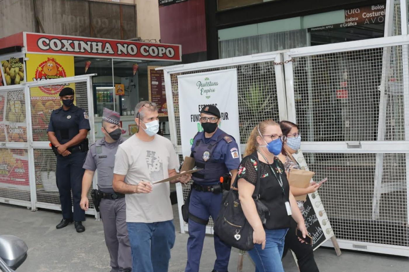 fiscais e guardas andam de máscara na calçada, um deles com prancheta #paratodosverem