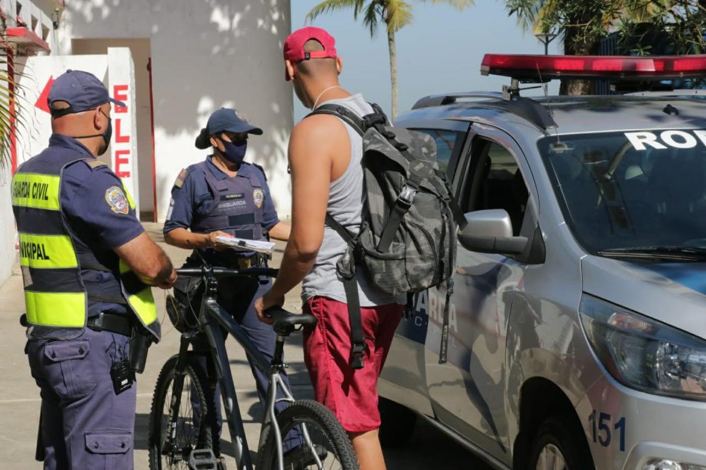 Guardas conversam com homem que está parado ao lado de bicicleta. #Paratodosverem