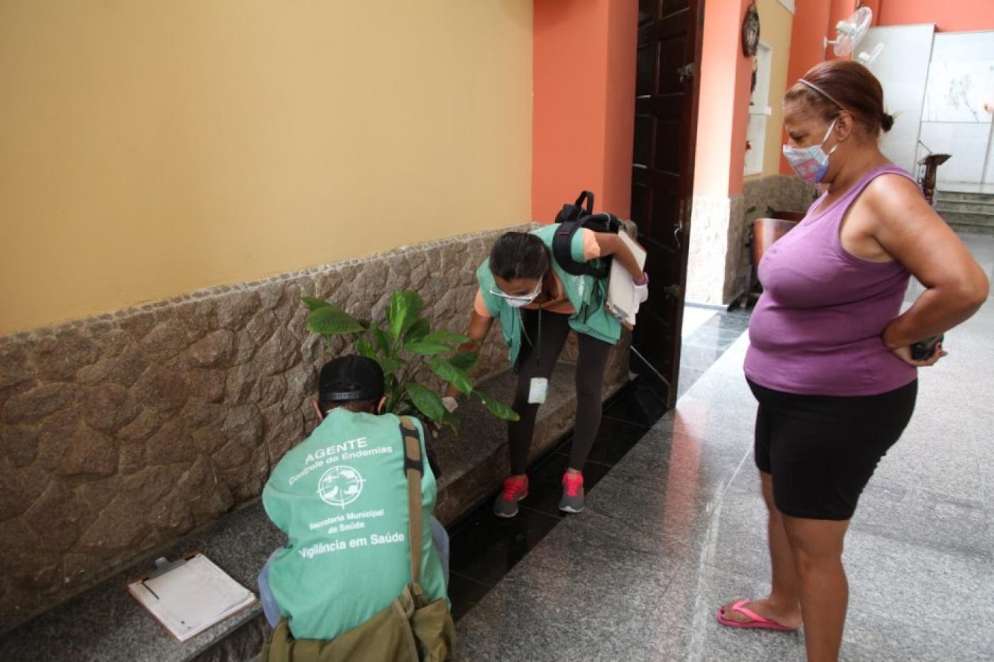 dois agentes olham vaso observados por mulher #paratodosverem 