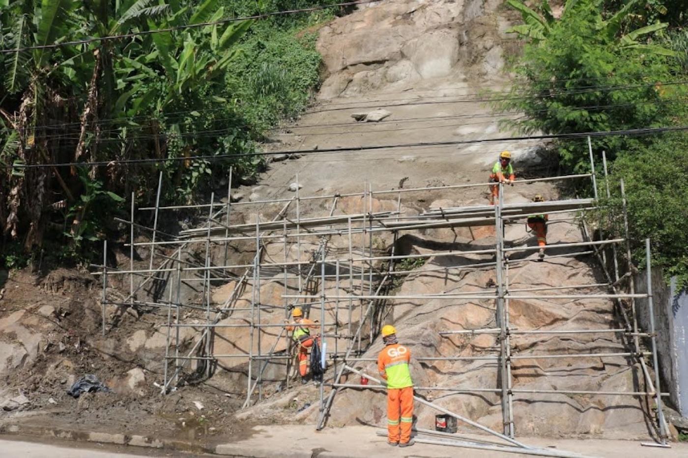 estrutura presa a rocha em encosta de morro com homens trabalhando. #paratodosverem
