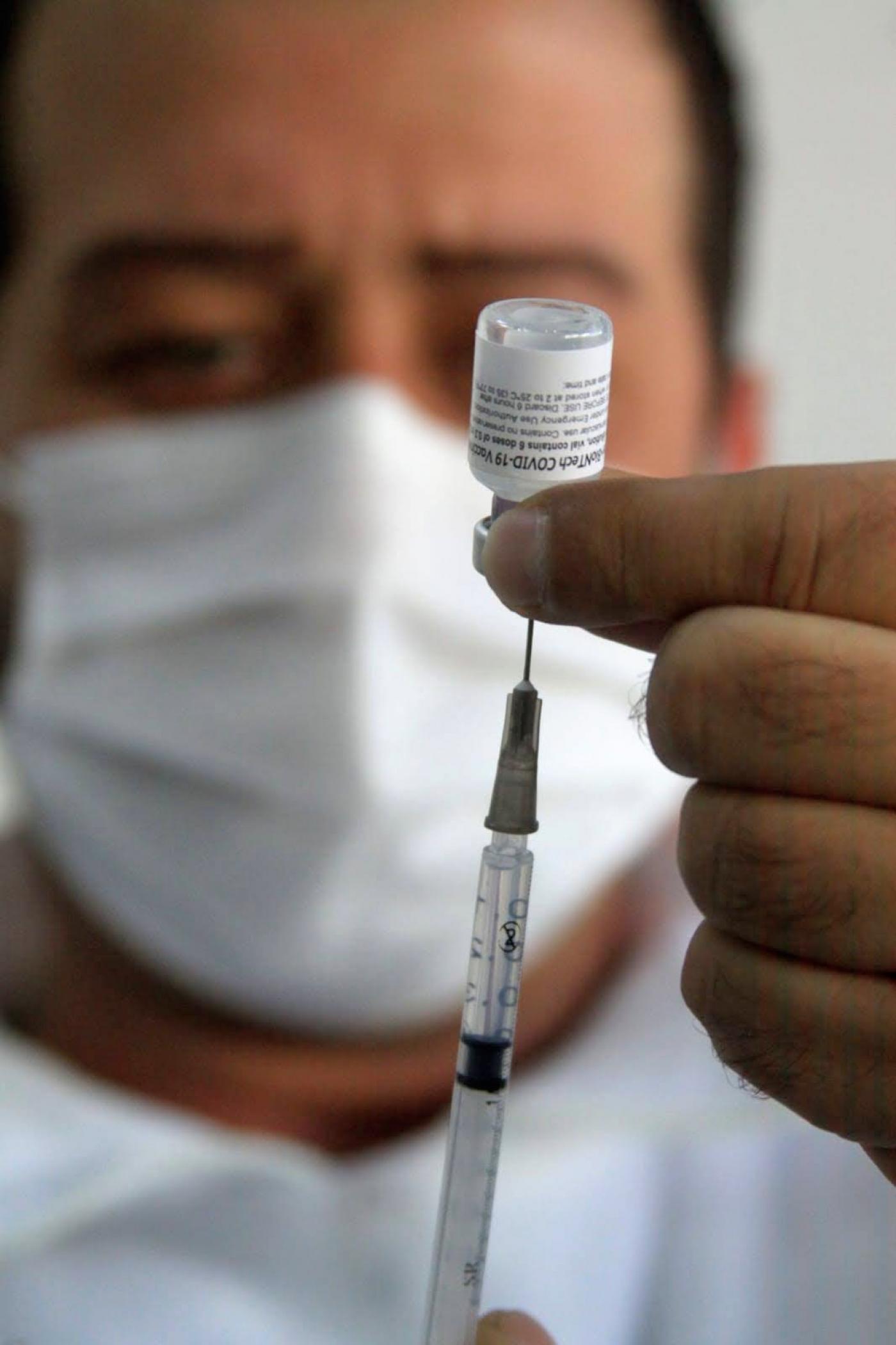 #pracegover enfermeiro injeta seringa em frasco de vacina