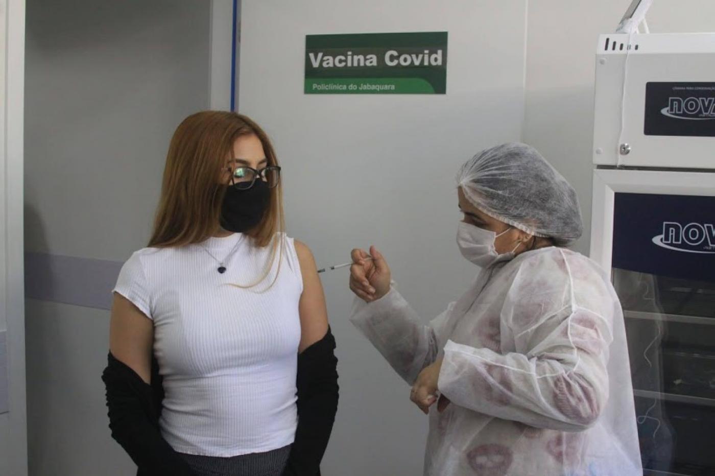 Jovem recebe aplicação da vacina. #paratodosverem