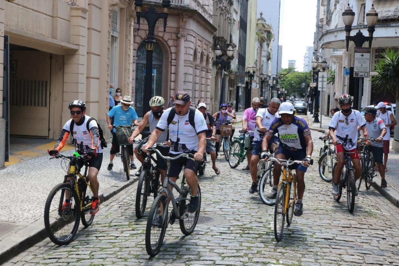 Pessoas andando de bicicleta em via do centro histórico de santos #paratodosverem